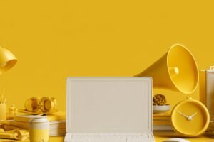 Com triar una agència de màrqueting digital per a la pime Escriptori de treball groc amb un portàtil obert, un megàfon i material d'oficina: què cal mirar abans de posar el màrqueting de la teva pime en mans d'una agència